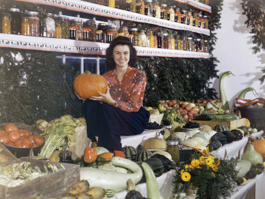 Teen with a Pumpkin Sits on a Shelf of Gourds at a Farmer's Market