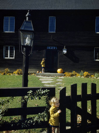 Girl Opens a Gate of a Colonial House Decorated with Pumpkins